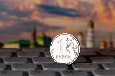 A coin in denomination of 1 ruble stands on a computer keyboard against the background of the Moscow Kremlin
