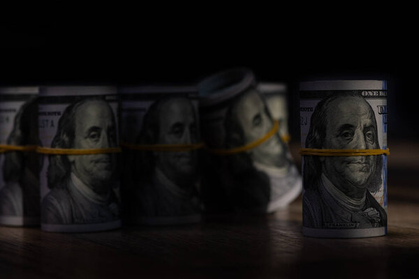 Rolled up 100 american dollar bills on wooden boards in light and shadow pattern