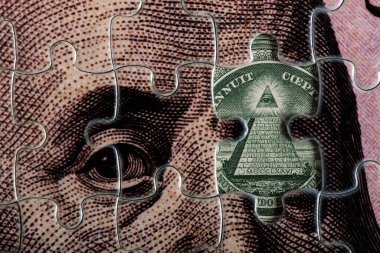 Jigsaw puzzle with a portrait of Benjamin Franklin from a 100 US dollar bill and a fragment of a 1 US dollar bill with a pyramid and an all-seeing eye