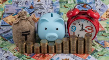 Conceptual plot about Kazakhstani currency - tenge with piggy bank, money bag, alarm clock, coins and banknotes