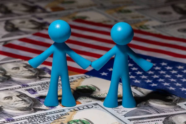 Two symbolic figurines of men against the background of the American flag and banknotes of 100 US dollars