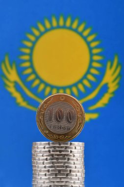 Coin in denomination of 100 Kazakhstani tenge against the background of a fragment of the Kazakhstani flag with a flying eagle and the Sun