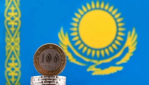 Coin in denomination of 100 Kazakhstani tenge against the background of a fragment of the Kazakhstani flag with a flying eagle and the Sun