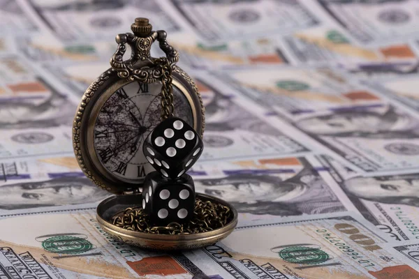 Dice and an antique pocket watch against the background of 100 US dollar bills