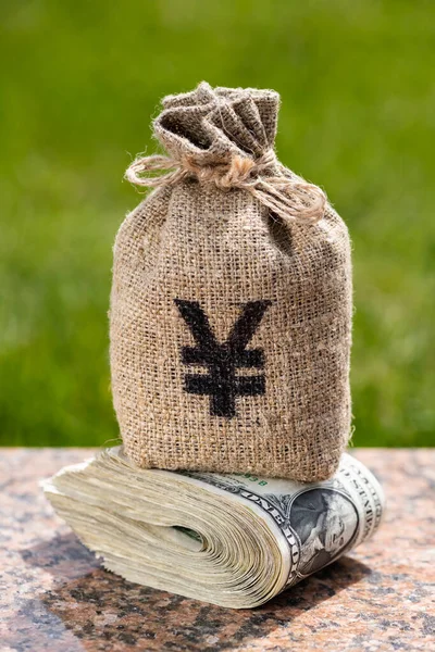 A money bag with a Chinese yuan symbol sits on top of a stack of 1 US dollar bills.