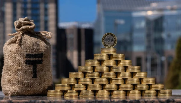 100 Kazakistan madeni para piramidi ve modern binaların arka planında bir tenge sembolü olan bir para çantası.