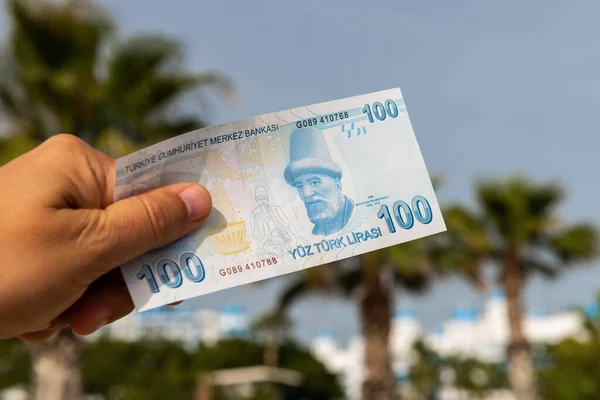 stock image Banknote in denomination of 100 Turkish liras in a man's hand on the background of a Turkish landscape