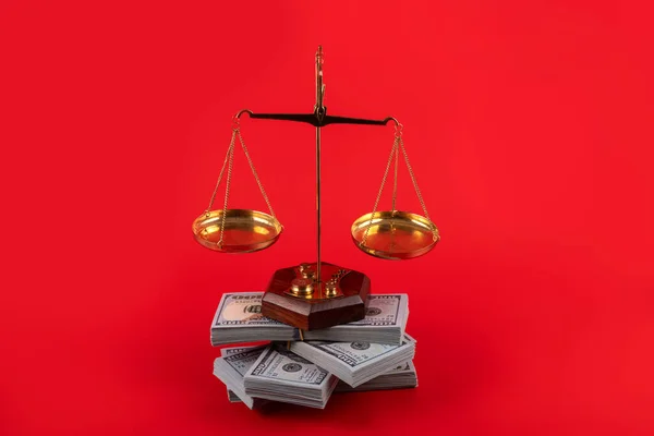 Golden scales and a large stack of 100 American dollars bills on a red background
