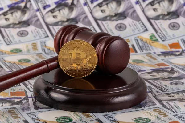 stock image A golden coin with the Bitcoin cryptocurrency symbol and a judge's gavel on the background of many 100 US dollar bills