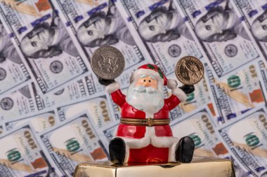 Bir elinde Noel Baba 'nın seramik biblosu bir elinde 1 dolar, diğerinde de yarım dolar, dolar ve altın külçelere karşı.