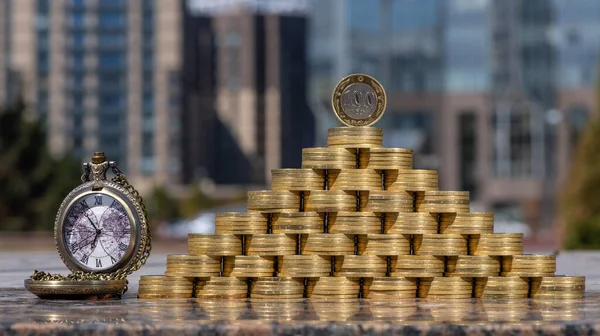 Pyramid of 100 Kazakhstani tenge coins against the background of modern buildings