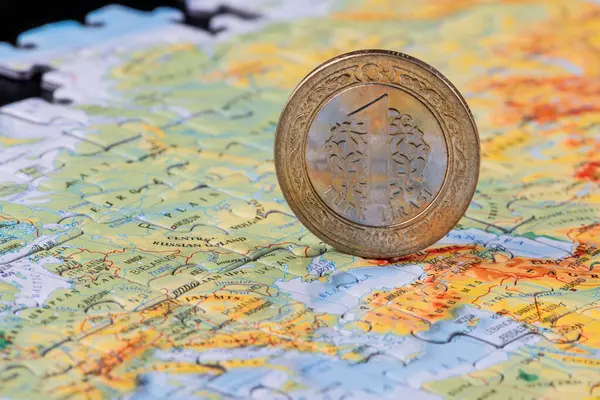1 Turkish lira coin against the background of a map of Europe and Asia, assembled from puzzles