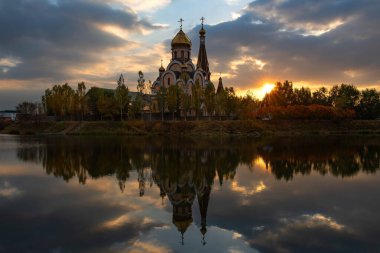 Gün batımında Kazak şehri Almaty 'de bir göletin kıyısındaki ortodoks kilisesi.