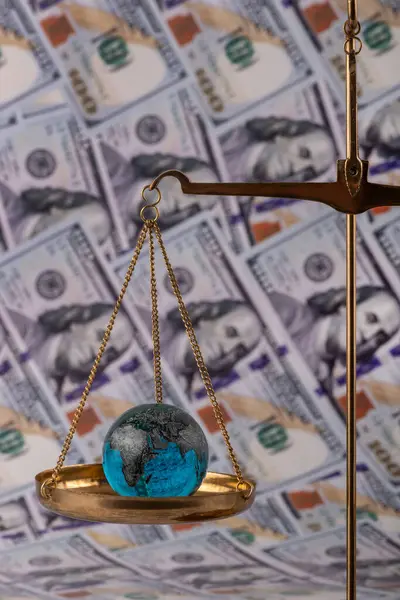 stock image Glass miniature globe on the scales against the background of banknotes in denominations of 100 American dollars