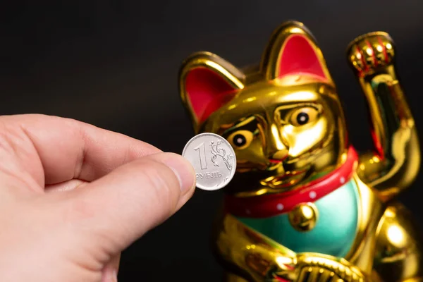A symbolic figurine of a Chinese cat that brings wealth and a coin of 1 Russian ruble