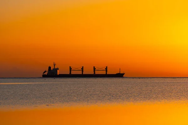Silhouette of a container ship sailing on the waves of the Red Sea during sunrise. The Red Sea is one of the busiest shipping routes in the world.