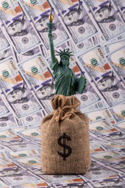 100 dolarlık banknotların arka planında Amerikan doları sembolü olan Özgürlük Heykeli ve para çantası.