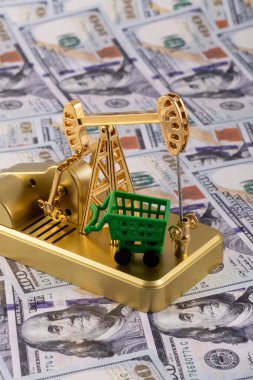 Altın minyatür yağ pompası ve 100 dolarlık banknotlarla dolu alışveriş arabası.