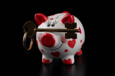 Komik domuz kumbarası ve siyah arka planda altın anahtar.