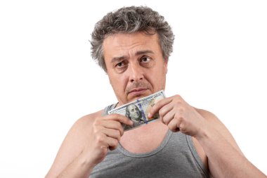 Kirli sakallı, beyaz saçlı, kolsuz tişört giyen orta yaşlı bir adamın elinde 100 dolarlık banknot var.