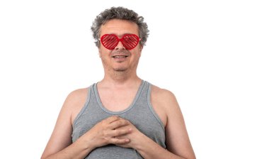 Gri saçlı, tüylü, traşsız orta yaşlı, kolsuz tişörtlü, güneş gözlüğü takan, insan kalbi şeklinde bir adam.