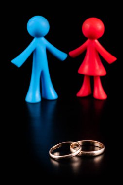 Altın alyanslar ve siyah arka planda bir erkek ve bir kadının sembolik figürleri.