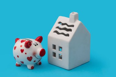 Mavi arka planda komik domuz kumbarası ve seramik sembolik ev