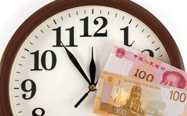 100 Çin yuanı ve 100 Rus rublesinin banknotları bir saatin arka planına karşıdır.