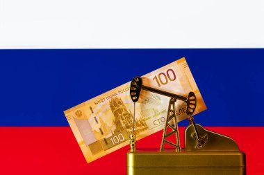 Altın minyatür petrol pompası ve Rusya Federasyonu bayrağının arka planına karşı 100 Rus rublesi.