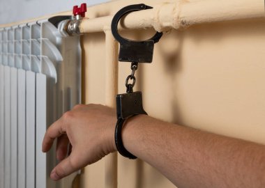 A man's hand in handcuffs closed on a radiator pipe clipart