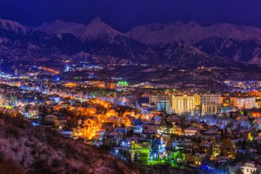 Kazak şehri Almaty 'nin üst kısmının kuş bakışı görüntüsü bir kış gecesinde bir dağ sırasının arka planına karşı.