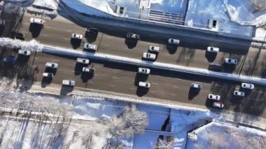 Güneşli bir kış gününde, şehir yolu olan ve arabaları hareket ettiren donmuş bir nehrin üzerindeki bir köprünün kuadkopter görüntüsü.