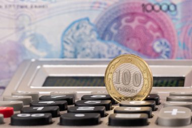 100 Kazakistan 10,000 tenge 'lik banknotun arka planında madeni para ve hesap makinesi var.