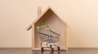 Symbolic wooden house and empty shopping cart from supermarket