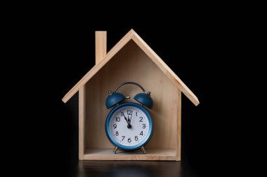 Siyah arka planda sembolik ahşap ev ve alarm saati