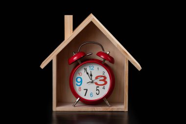 Siyah arka planda sembolik ahşap ev ve alarm saati