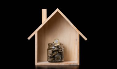 Minyatür ahşap ev ve siyah arka planda 100 ve 200 Kazakistan paralı cam kavanoz.