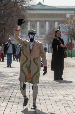 Almaty, Kazakistan, 03.21.2025. Bir bahar günü Kazak şehrinin caddesinde geleneksel Kazak kıyafetleri içinde bir android robot.