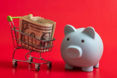 Mavi domuz kumbarası ve kırmızı arka planda 1 dolarlık alışveriş arabası.
