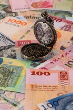 Dünyanın farklı ülkelerinden gelen çeşitli banknotların arka planında zincirli cep saati