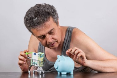 Gri saçlı, orta yaşlı bir adamla yoksulluk hakkında kavramsal bir hikaye. 100 Euro 'luk banknot ve süpermarketten alınmış minyatür alışveriş arabası.
