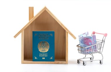 Minyatür ahşap ev, Kazakistan vatandaşının pasaportu ve beyaz arka planda minyatür alışveriş arabasında 10.000 Kazakistan parası.