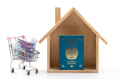 Minyatür ahşap ev, Kazakistan vatandaşının pasaportu ve beyaz arka planda minyatür alışveriş arabasında 10.000 Kazakistan parası.