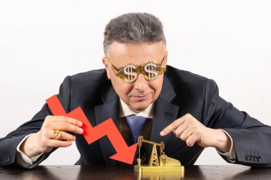 İş elbisesi giymiş orta yaşlı bir adamla düşen petrol fiyatları, düşen fiyat tablosunun kırmızı oku ve minyatür bir petrol pompasıyla ilgili kavramsal bir hikaye.