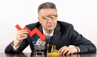 İş elbisesi giymiş orta yaşlı bir adamla düşen petrol fiyatları, düşen fiyat tablosunun kırmızı oku ve minyatür bir petrol pompasıyla ilgili kavramsal bir hikaye.