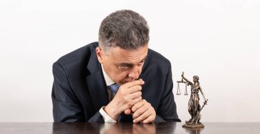 Aynı yaşlarda, takım elbiseli ve Themis figürlü bir adam.