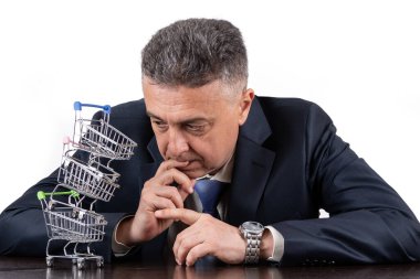 Takım elbiseli orta yaşlı bir adam ve boş minyatür market arabaları piramidi.