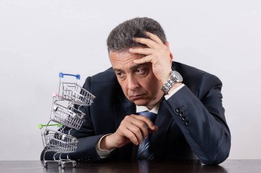 Takım elbiseli orta yaşlı bir adam ve boş minyatür market arabaları piramidi.