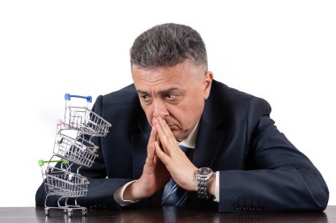 Takım elbiseli orta yaşlı bir adam ve boş minyatür market arabaları piramidi.