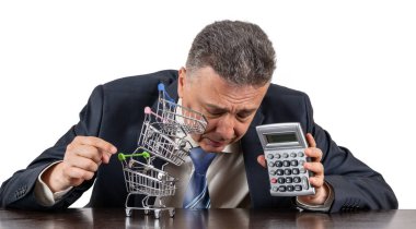 Takım elbiseli orta yaşlı bir adam, domuzcuk bnk ve boş minyatür market arabalarından oluşan bir piramit.